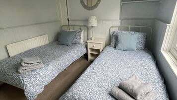 A bedroom with two single beds, a bedside table with a lamp, a mirror on the wall, and a shelf with small plants.
