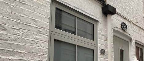 Een wit gebouw met een raam, een deur en een zwarte brievenbus, met een plantje voorop.