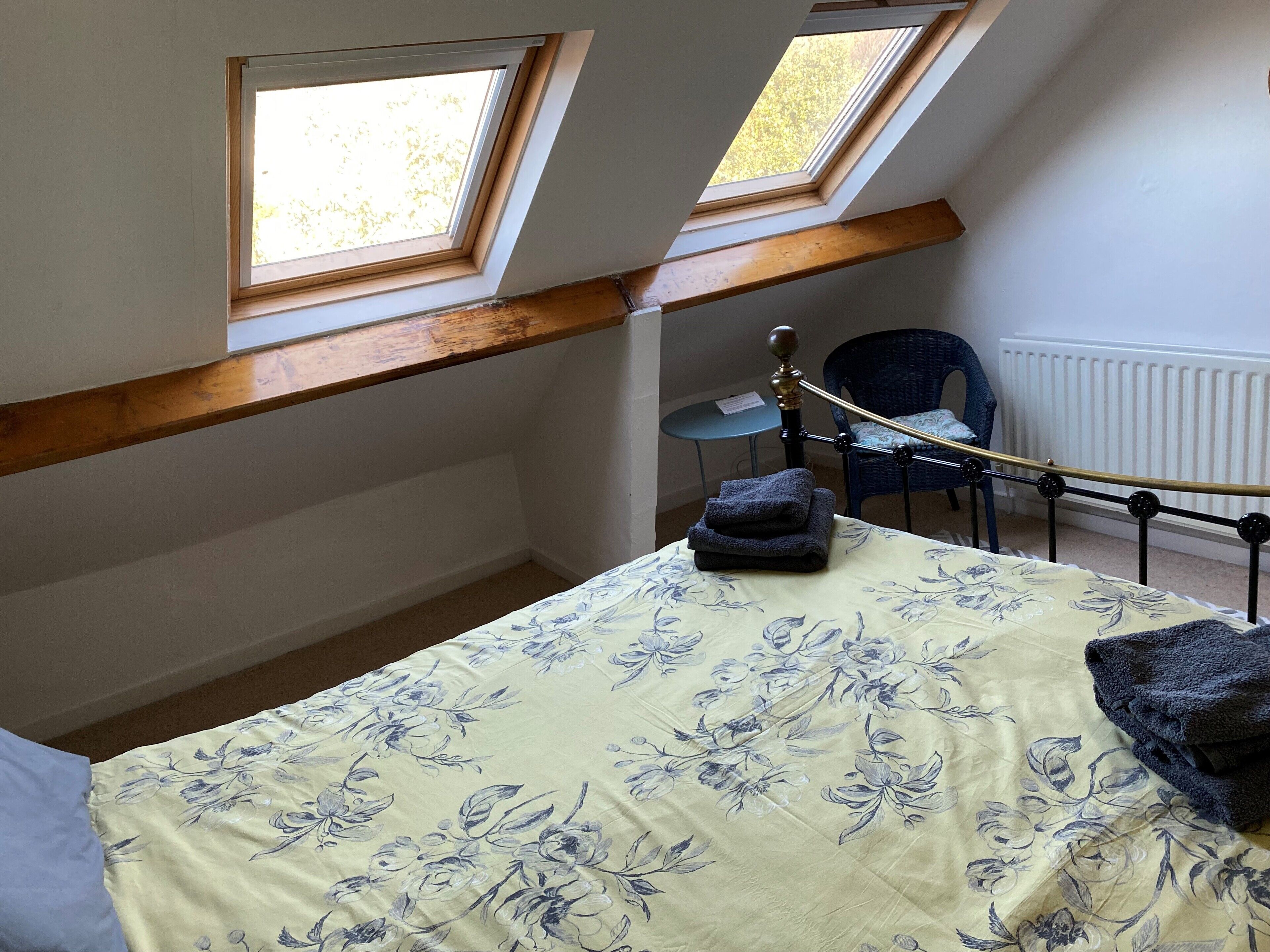 Een slaapkamer met een bed, twee dakramen, een stoel en een radiator.