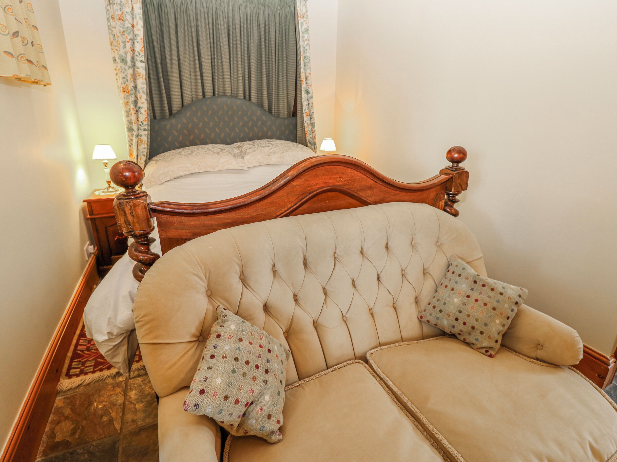 A bedroom with a bed, a sofa, a nightstand, and a lamp.