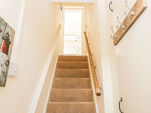 A carpeted staircase with a wooden handrail, a door at the top, and a wall-mounted metal coat rack. - Oak Lodge (Cromer)