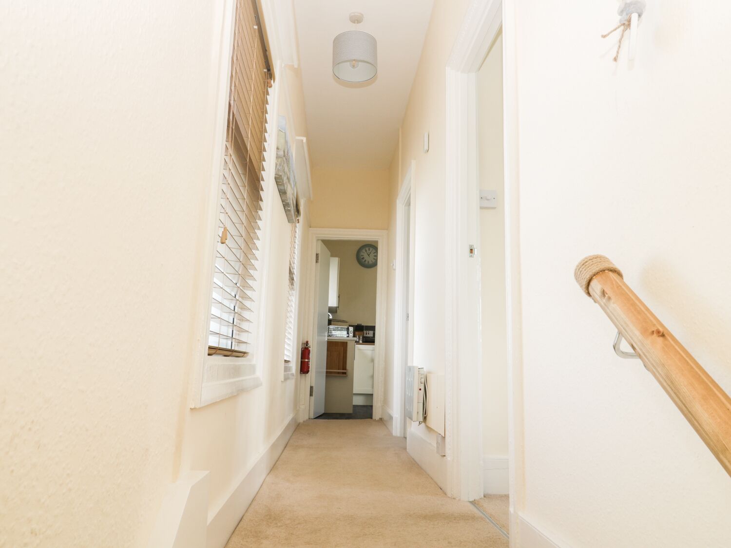 A narrow hallway with a carpeted floor, white walls, and a wooden handrail on the right.