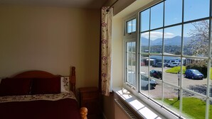 Un dormitorio con cama, ventana y vista a un estacionamiento y montañas.