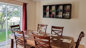 Un comedor con una mesa y sillas de madera, una puerta de cristal que da al exterior y una estantería con copas de vino.