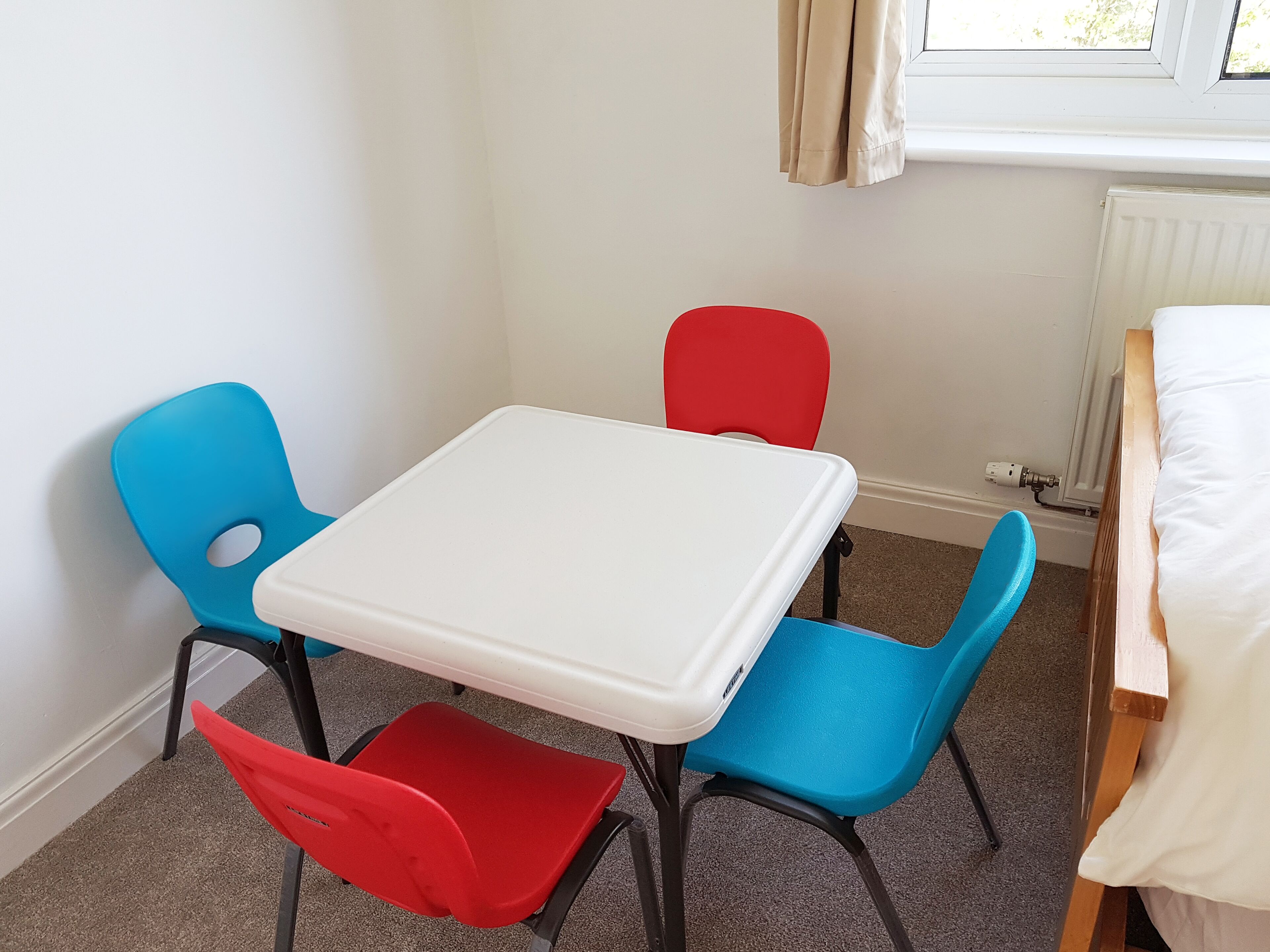 A small room with a white table and four chairs in red, blue, and blue.