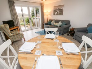 Relax in this inviting living space with a dining table for four, comfortable seating area, and a large sliding glass door leading to a garden view.