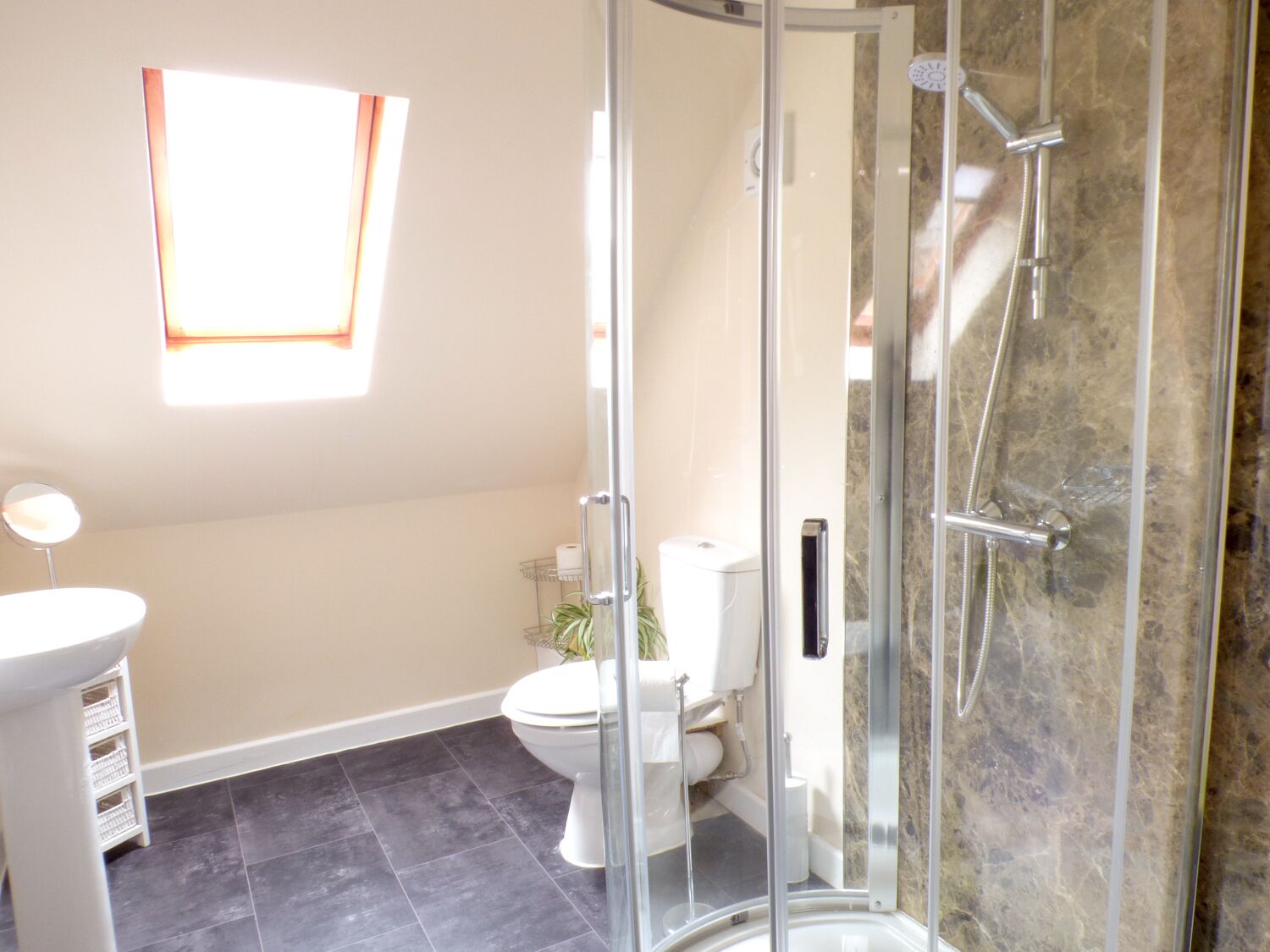 A bathroom with a glass-enclosed shower, a toilet, a sink, and a window providing natural light.
