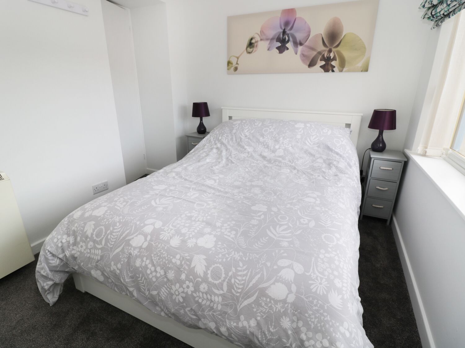 A neatly made bed with a floral-patterned bedspread, two bedside tables with lamps, and a window with curtains.