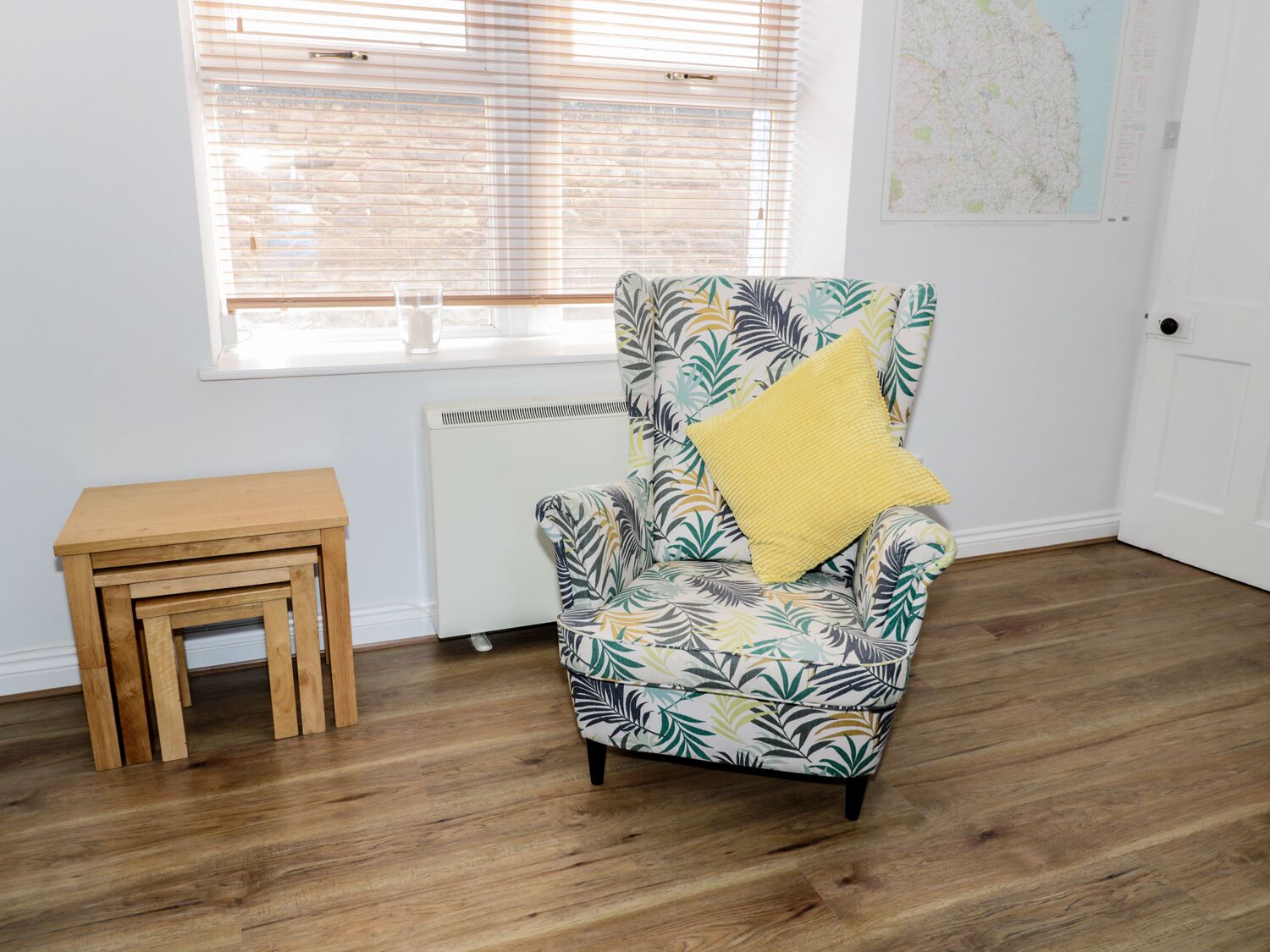 Une pièce avec un fauteuil à motifs, une petite table en bois et un radiateur.