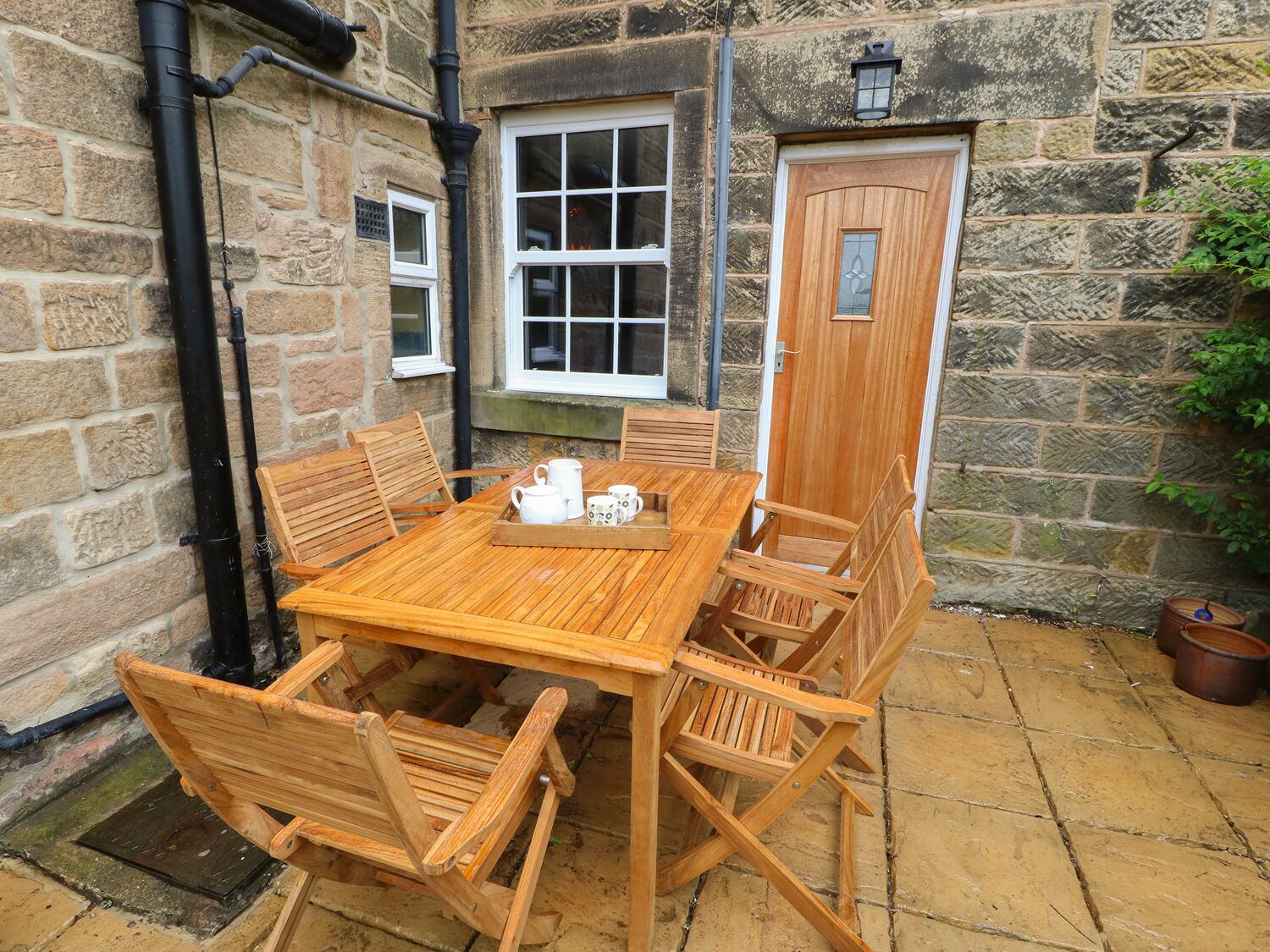 A wooden table and chairs set up on a stone patio with a stone wall and a wooden door.
