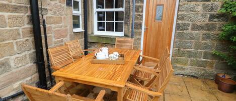 A wooden table and chairs set up on a stone patio with a stone wall and a wooden door.