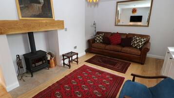 Una sala de estar con chimenea, un sofá, una mesa de centro, un sillón azul y un tapete estampado.