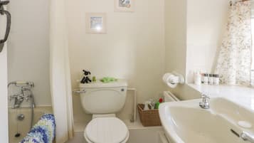 A bathroom with a toilet, bidet, and sink. There are two framed pictures on the wall, a basket with toiletries, and a shower curtain.