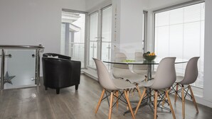 Ett modernt matområde med ett glasbord, fyra stolar och en svart soffa.