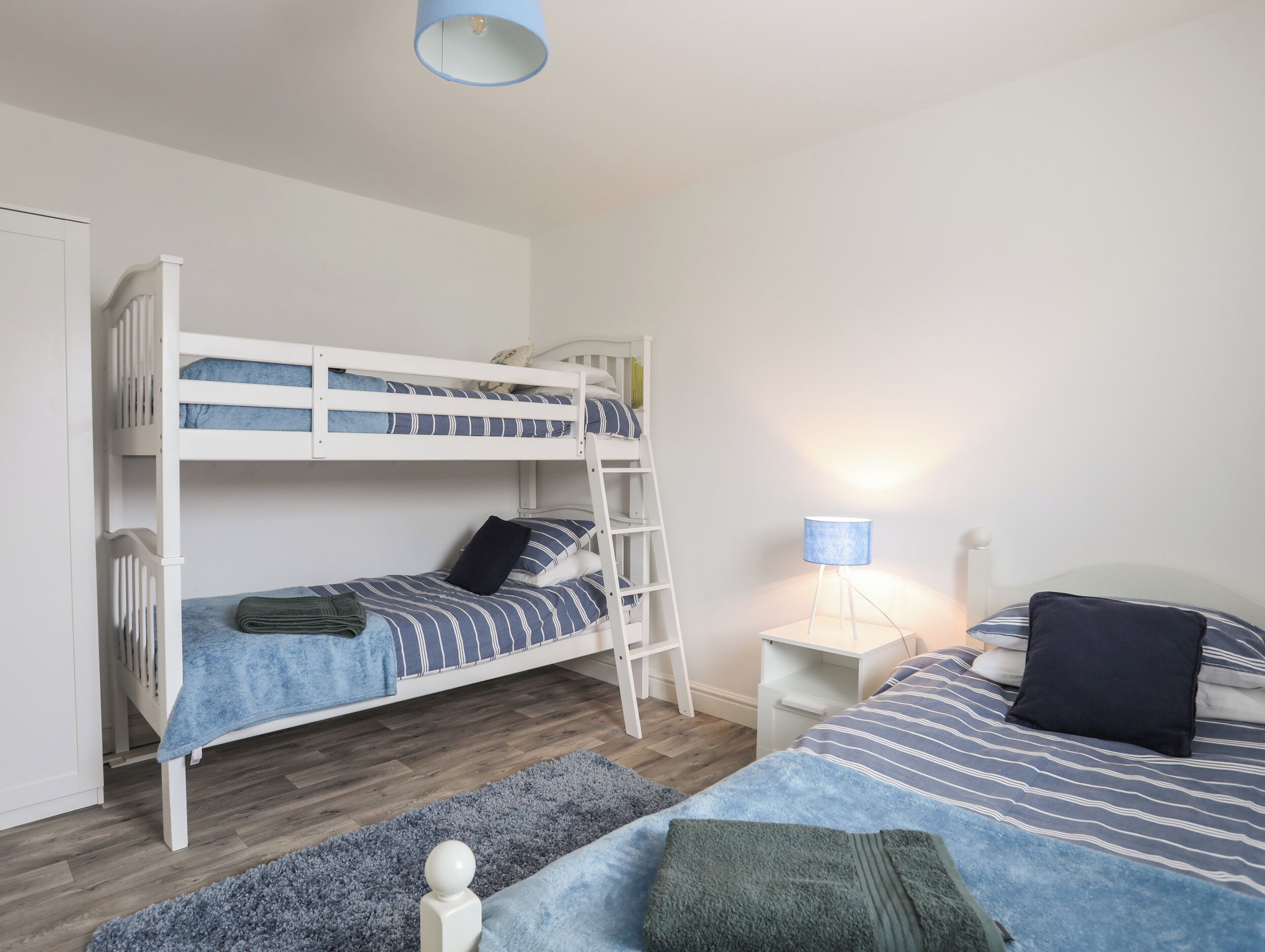 A bunk bed with a ladder, a bedside table with a lamp, and a separate bed with pillows and a blanket.