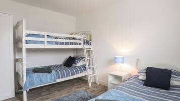 A bunk bed with a ladder, a bedside table with a lamp, and a separate bed with pillows and a blanket.