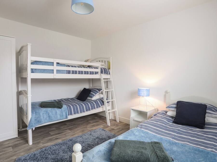 A bunk bed with a ladder, a bedside table with a lamp, and a separate bed with pillows and a blanket.