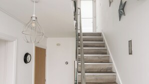 En trappa med trästeg och ett metallräcke, en vit vägg med en klocka och en hängande lampa.