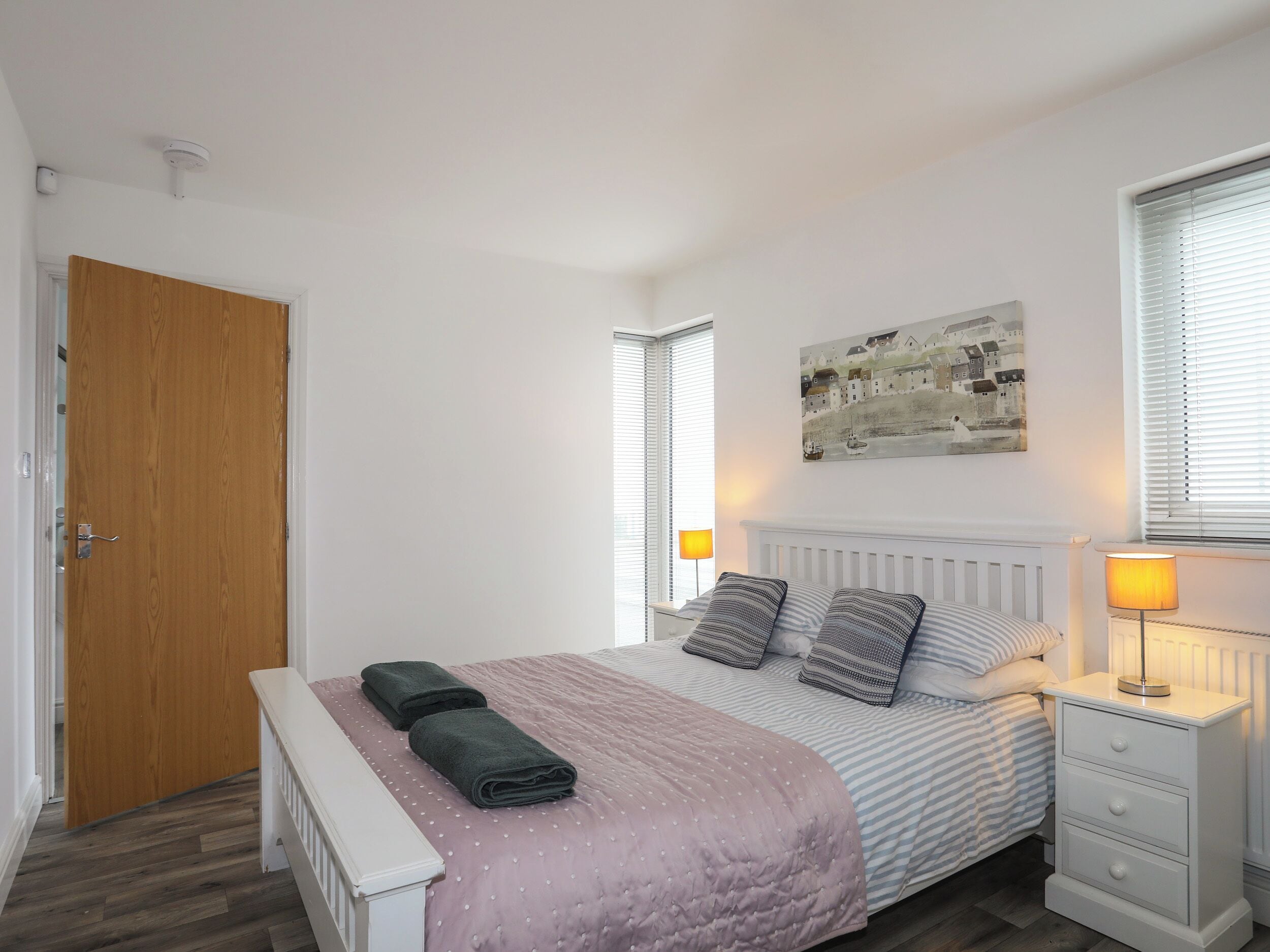 A bedroom with a bed, bedside table, lamp, and a painting on the wall.