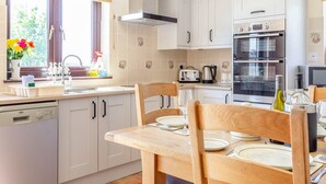 Una cocina moderna con armarios blancos, lavavajillas, horno doble y comedor con sillas de madera y una mesa dispuesta para dos.