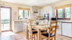 Una cocina moderna con armarios blancos, lavavajillas, microondas y estufa. Hay una mesa de comedor con sillas y una ventana con persianas.