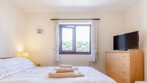 Un dormitorio con cama, cómoda, televisor y ventana con cortinas.