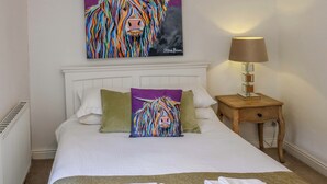 A hotel room with a bed, pillows, a nightstand with a lamp, and a painting of a colorful animal on the wall.