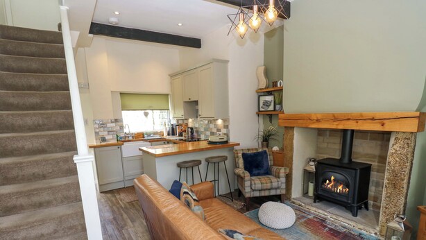 A modern living room with a brown leather sofa, a fireplace, and a kitchen area with a wooden island.