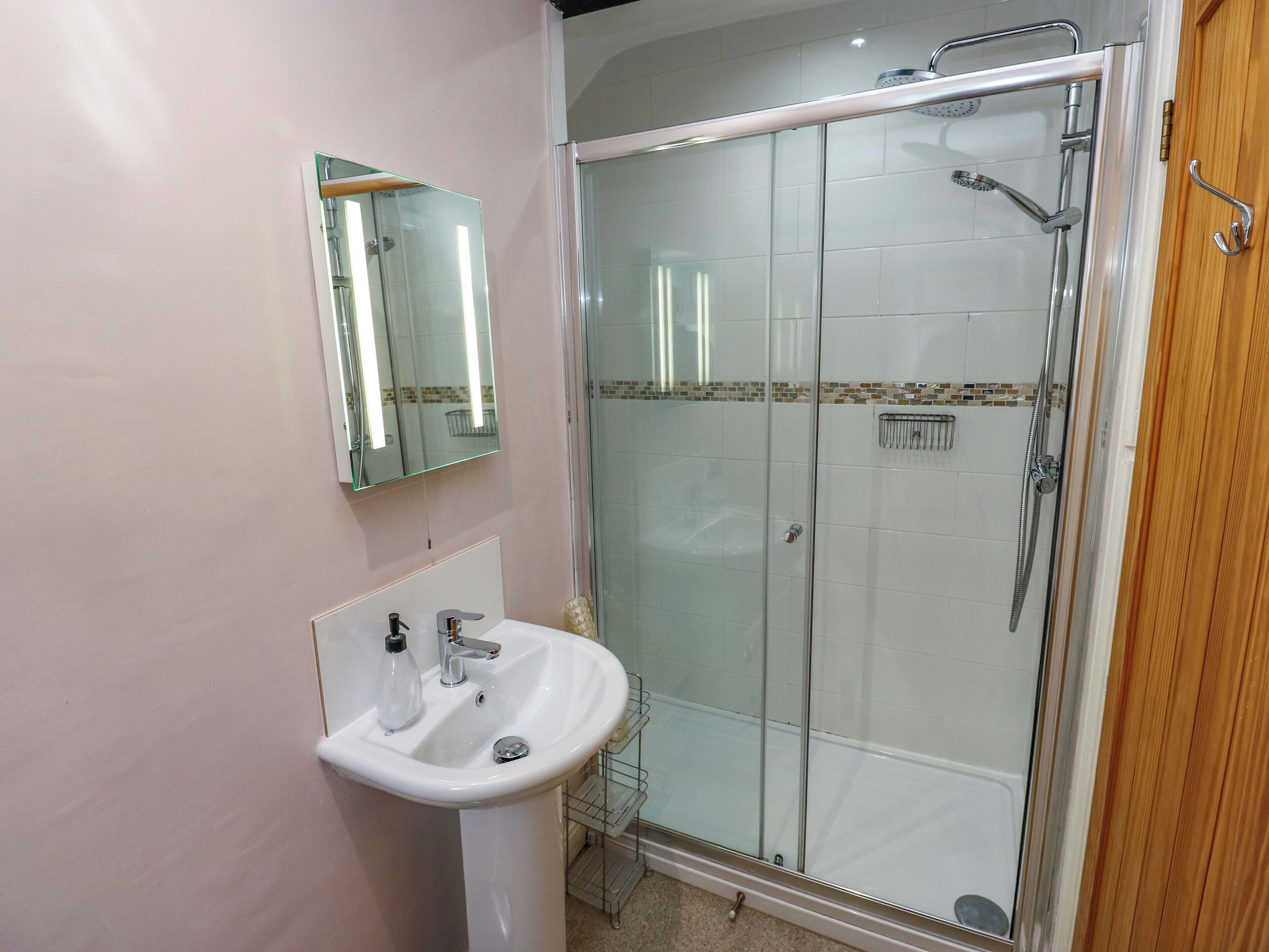 A bathroom with a glass-enclosed shower, a white sink, and a mirror.