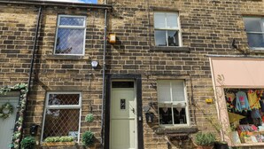 A two-story stone building with multiple windows, a door, and a small shop on the ground floor.