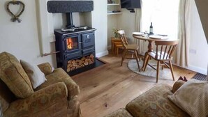 A cozy living room with a wood-burning stove, comfortable sofas, a dining table, and a TV. - Fells Cottage (Sedbergh)
