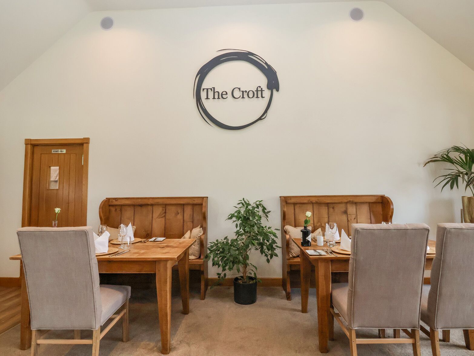 Et spiseområde med træborde og stole, en potteplante og et skilt med teksten "The Croft".