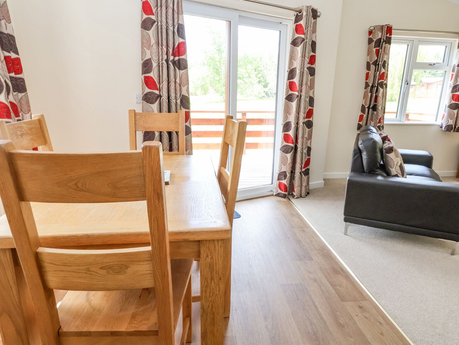 A dining area with wooden chairs and a table, a sofa, and patterned curtains.