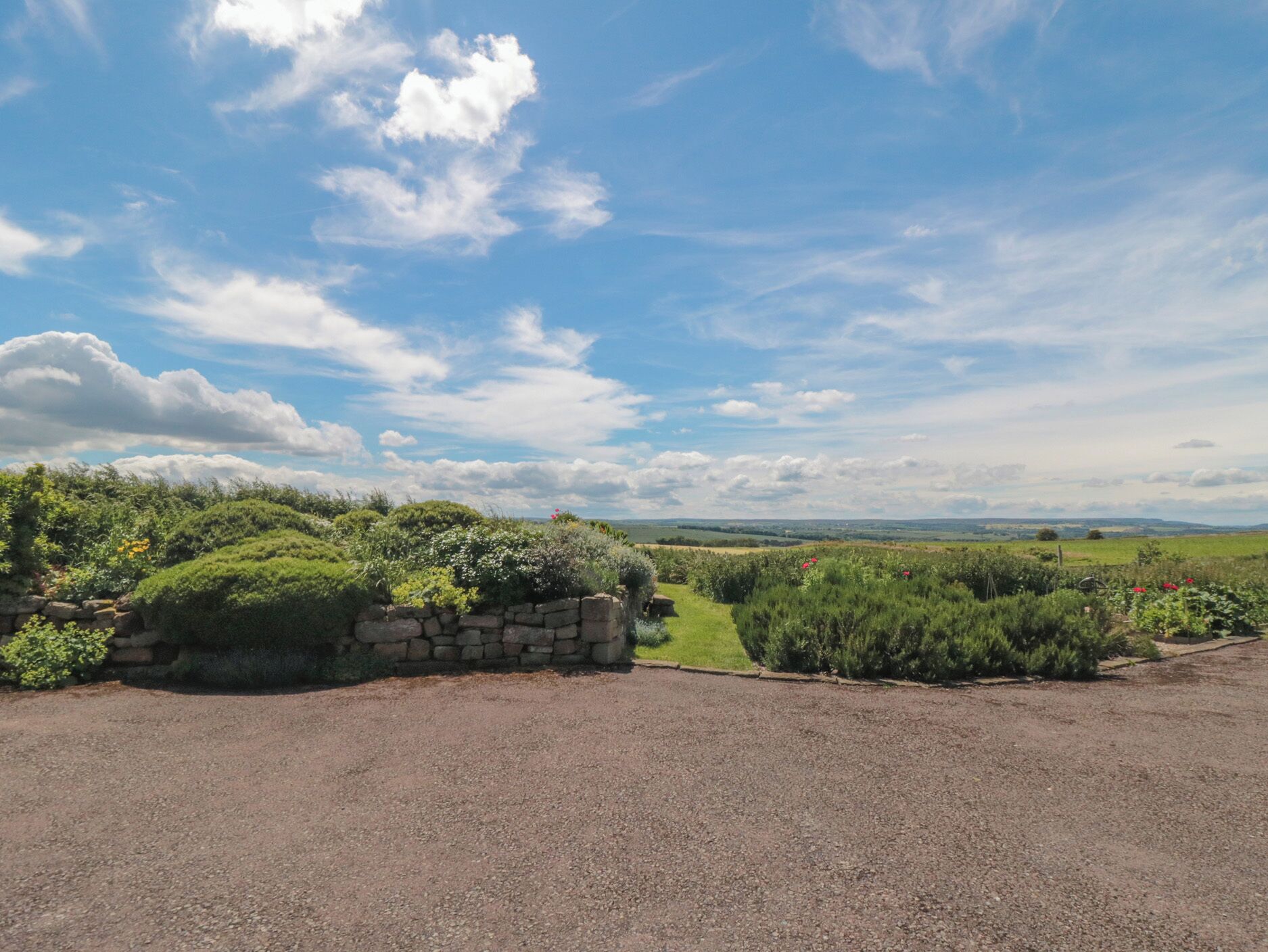 A rural landscape with a gravel path leading to a stone wall and lush greenery.