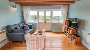 A living room with a sofa, armchair, wooden floor, bookshelf, and a television. - Field Cottage (Saltburn-by-the-Sea)