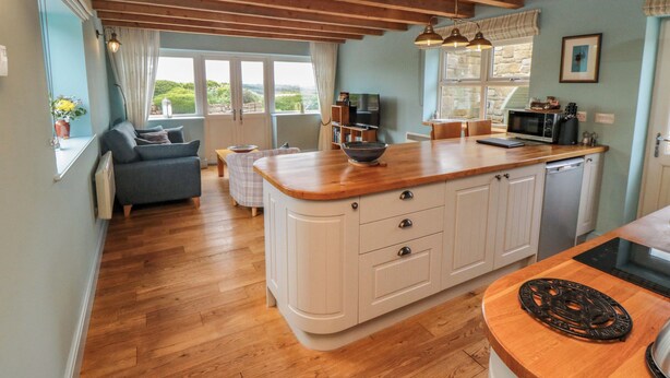 A modern kitchen with wooden flooring, a central island, and a dining area with a sofa. - Field Cottage (Saltburn-by-the-Sea)