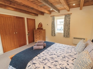 Ein Schlafzimmer mit einem Bett, einem Schminktisch, einem Fenster mit Vorhängen und Holztüren.