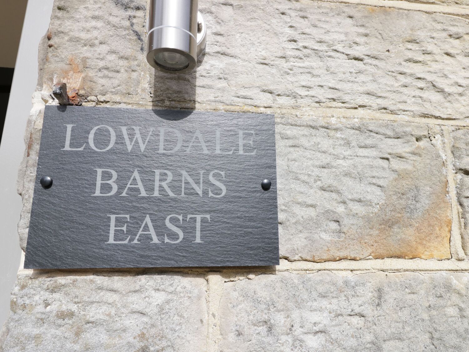 Een betonnen bordje met de tekst 'LOWDALE BARNES EAST', bevestigd aan een stenen muur.