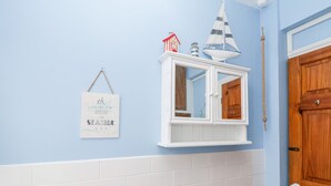 Ein Badezimmer mit hellblauer Wand, weiß gefliestem unteren Bereich, einer Holztür, einem weißen Schrank mit Spiegel und einem Schild mit der Aufschrift 'oh I do like to be beside the seashide'.