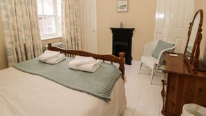 Ein Schlafzimmer mit Bett, Stuhl, Kommode, Kamin und Vorhängen.