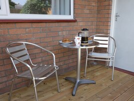 Un pequeño espacio al aire libre con dos sillas de metal y una mesa, una ventana y una puerta.