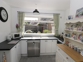 Cocina moderna con armarios blancos, lavavajillas de acero inoxidable, microondas y ventana con cortinas a cuadros.