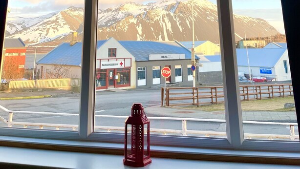 A window with a view of a mountain range, a stop sign, a red lantern, and a building with a blue roof. - Egils Studio Apartments (Borgarnes)