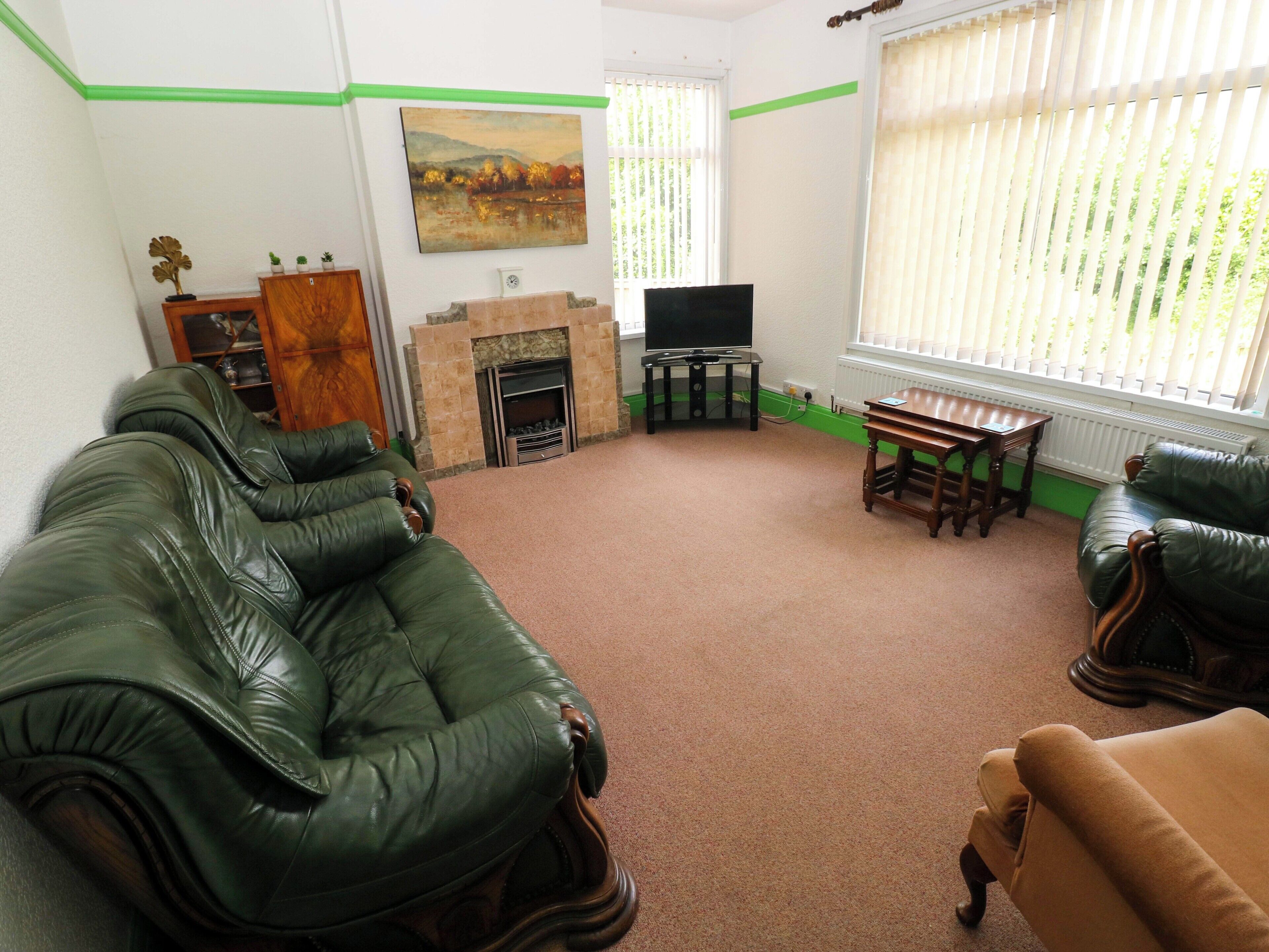 Una sala de estar con sofás de cuero verde, chimenea, televisor y ventana con persianas.
