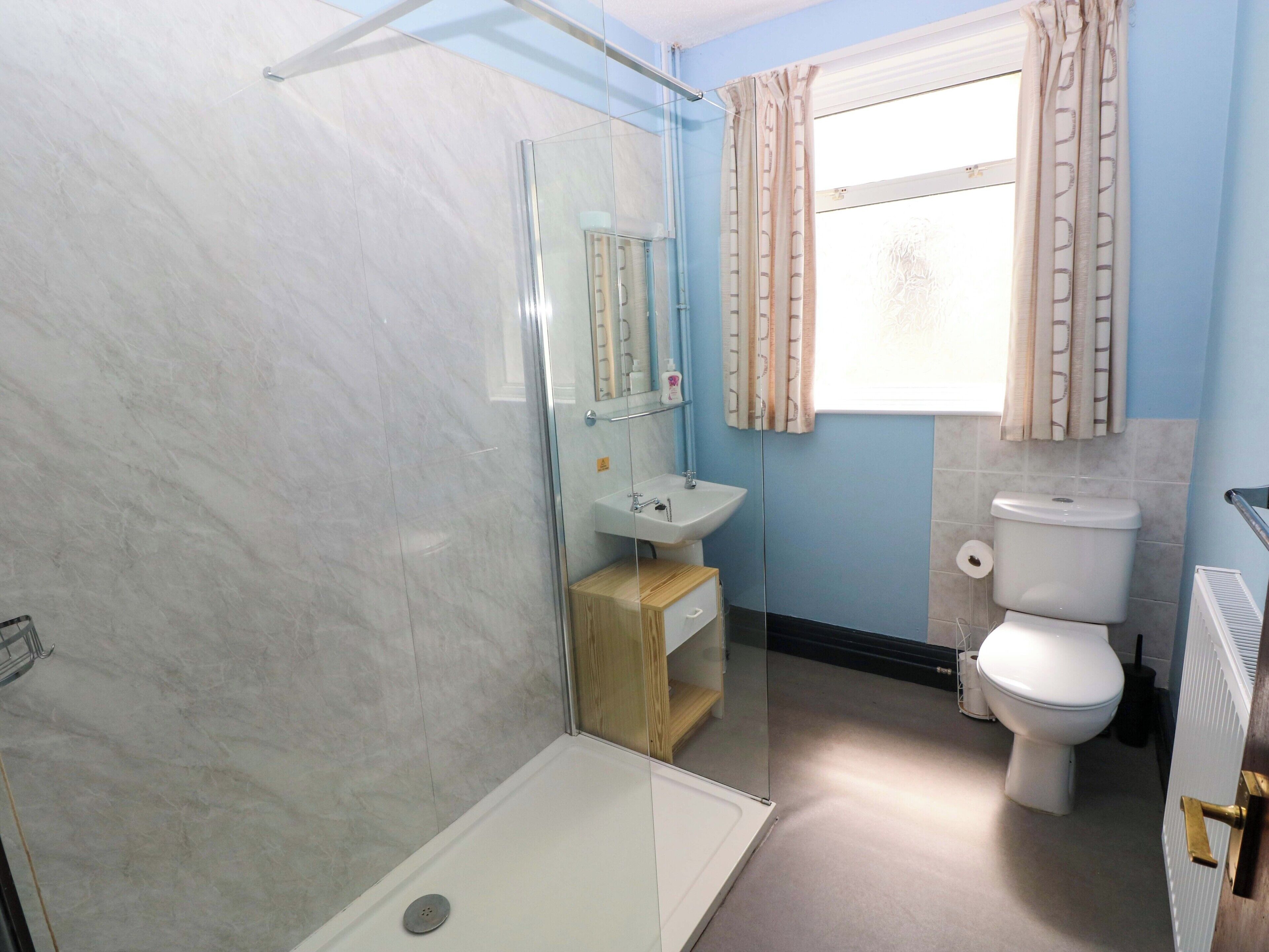A bathroom with a shower, sink, toilet, and a window with curtains.