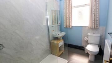 Un baño con ducha, lavamanos, inodoro y ventana con cortinas.