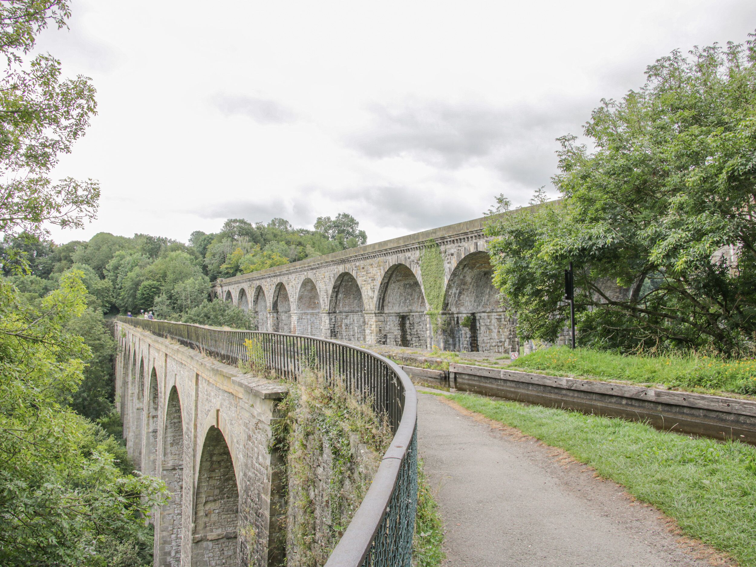 Un viaduc en pierre, doté de nombreuses arches, entouré d’une végétation luxuriante et d’arbres.