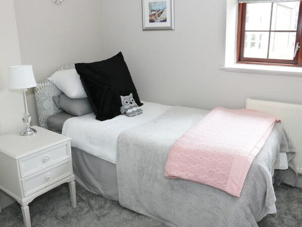 A neatly arranged bedroom with a bed, a bedside table with a lamp, a window, and a radiator.