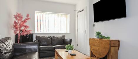 A modern living room with a leather sofa, a wooden coffee table, and a TV mounted on the wall.