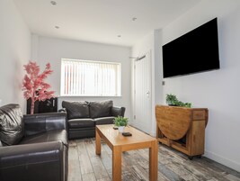 Una sala de estar moderna con un sofá de cuero, una mesa de centro de madera y un televisor montado en la pared.